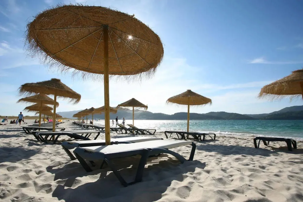 Transats et parasols de paille sur une plage de sable fin ensoleillée.