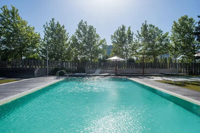 Une piscine rectangulaire turquoise entourée d'un sol en bois et de chaises longues.