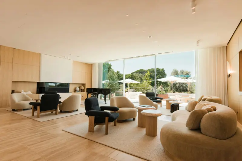 Un espace de détente intérieur avec des fauteuils et un piano près de grandes baies vitrées.