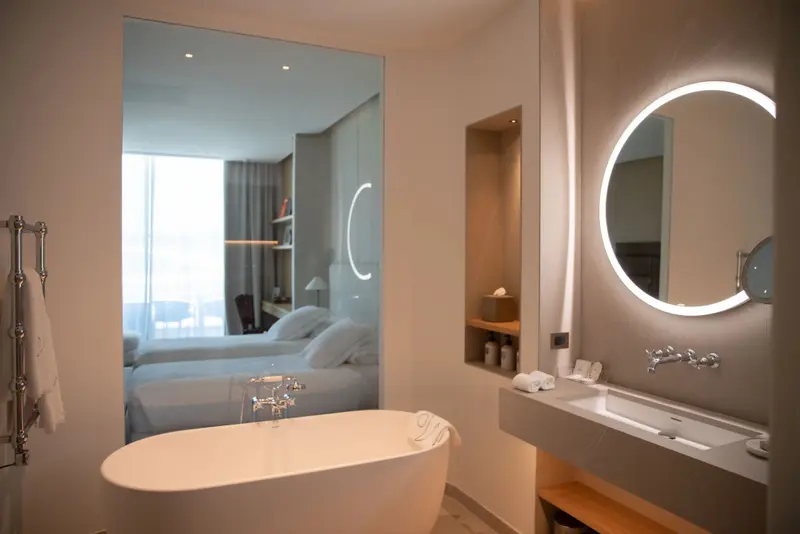 Une baignoire et un lavabo dans une salle de bain moderne avec une chambre visible en arrière-plan.
