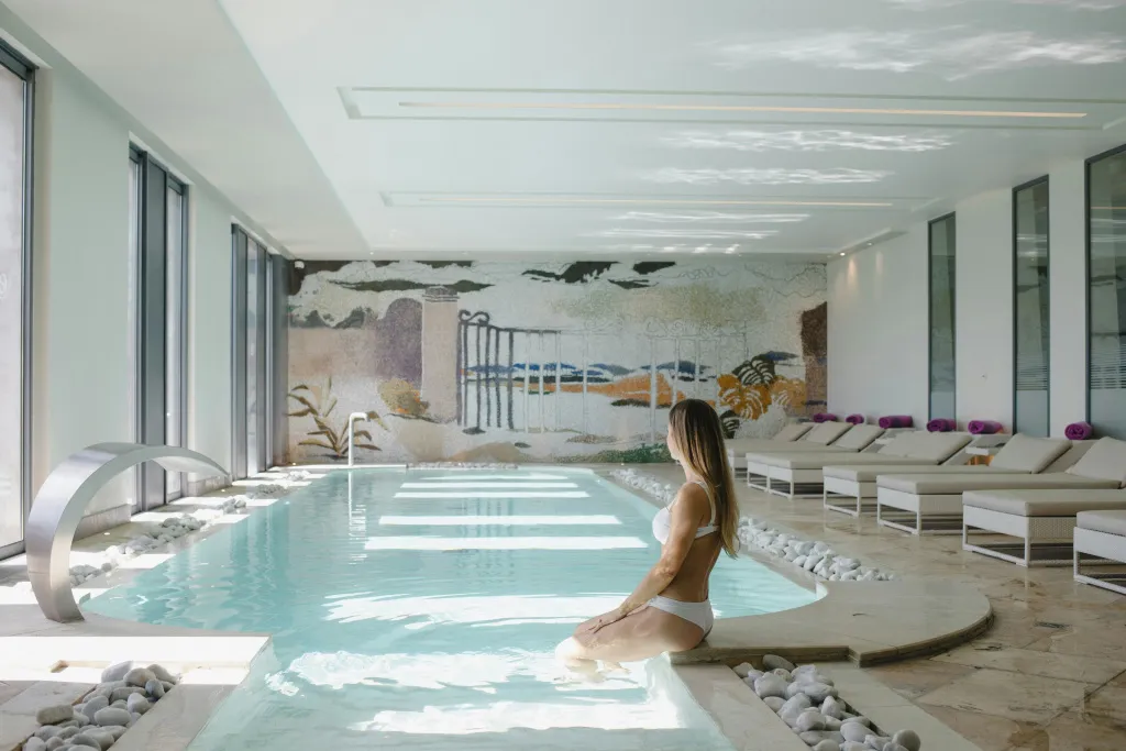Une femme se détend au bord d'une piscine intérieure lumineuse.