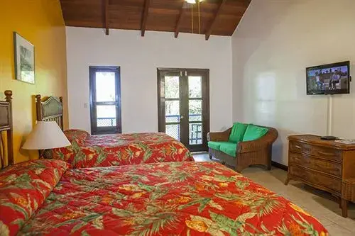 Une chambre lumineuse avec deux lits et un fauteuil en osier près d'une porte-fenêtre.