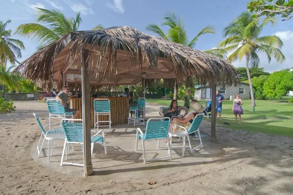 Un bar de plage ombragé avec des clients assis sur des tabourets et des chaises.