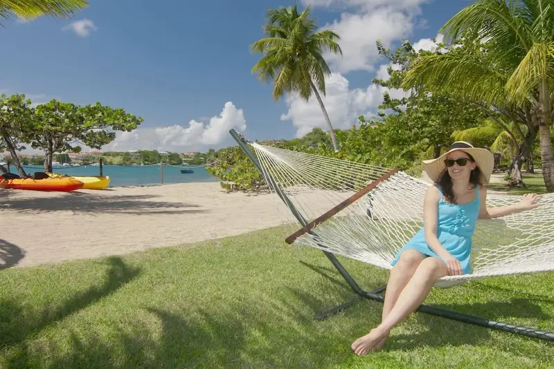 Une femme se détend dans un hamac sur une pelouse verdoyante face à une plage.