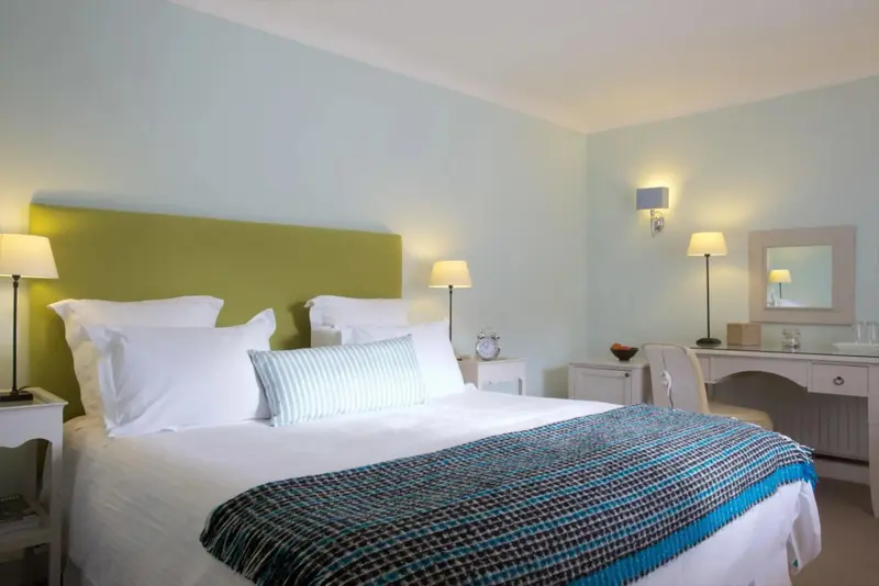 Une chambre lumineuse avec un grand lit recouvert d'une couverture colorée et un bureau coquet.