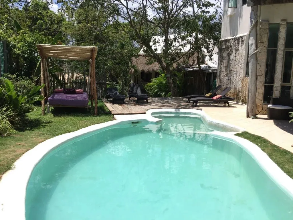Une piscine turquoise bordée d'une terrasse ensoleillée avec des chaises longues et un hamac.