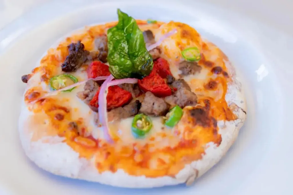 Une pizza garnie de légumes et de viande est présentée sur une assiette blanche.