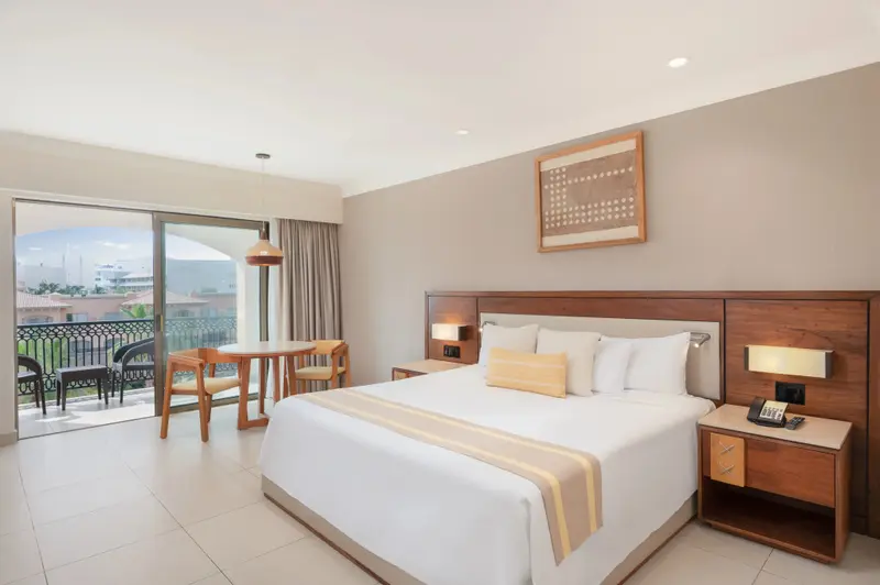 Une chambre lumineuse avec un lit double et un coin repas près d'une baie vitrée.