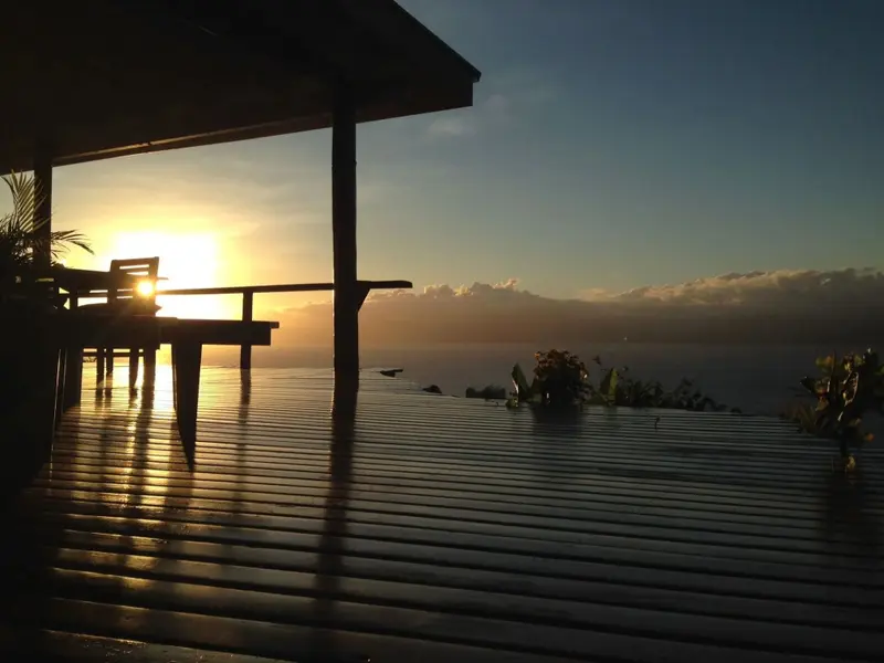Terrasse en bois avec mobilier donnant sur la mer au coucher du soleil.
