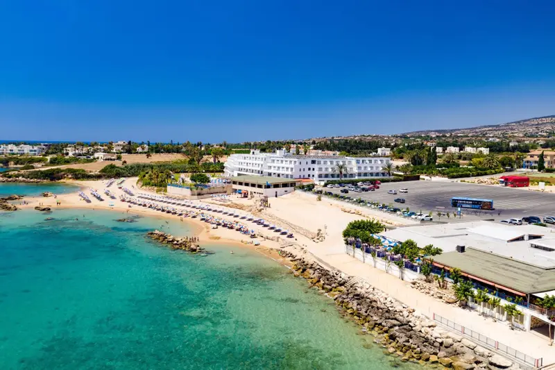 Vue aérienne d'une plage de sable fin bordée d'eaux turquoise et d'un bâtiment blanc.