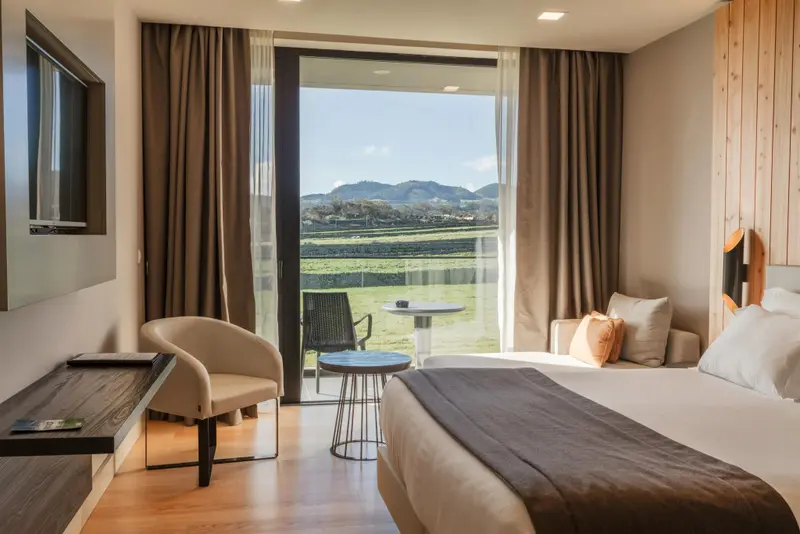 Une chambre lumineuse avec un lit confortable et un accès à une terrasse offrant une vue sur un paysage verdoyant.