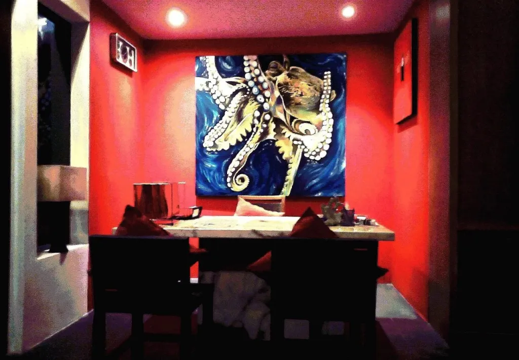 Une table est dressée devant une grande peinture marine dans une salle aux murs rouges.