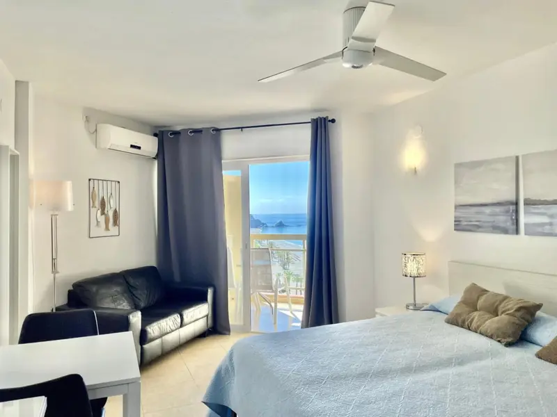 Une chambre lumineuse s'ouvre sur une vue mer depuis un balcon.