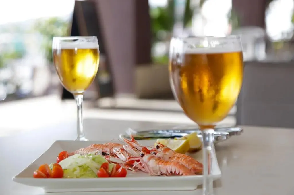 Une assiette de crevettes et deux verres de bière sont posés sur une table.
