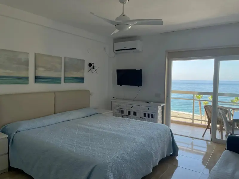 Une chambre lumineuse avec un grand lit face à une baie vitrée donnant sur la mer.