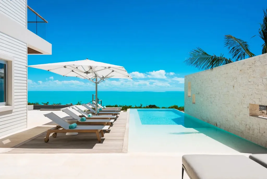Transats blancs alignés au bord d'une piscine à débordement avec vue sur la mer.