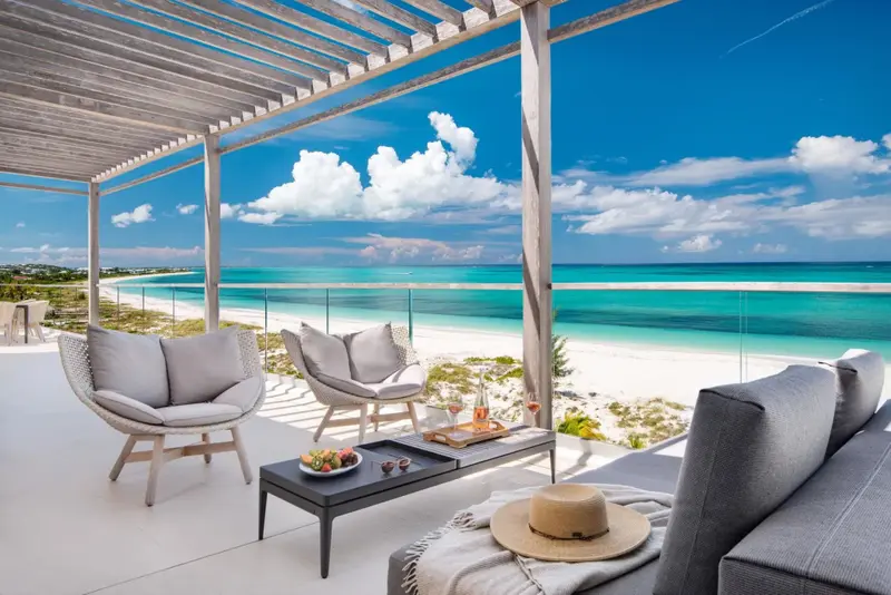 Espace de détente extérieur avec mobilier confortable face à une plage de sable blanc.