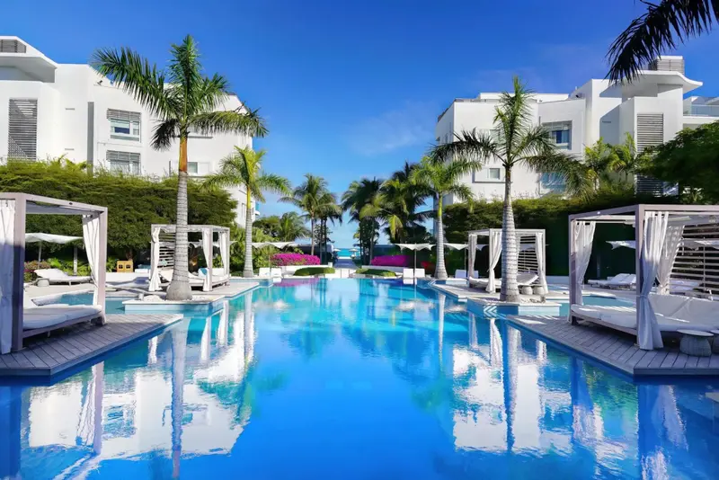 Une longue piscine turquoise bordée de palmiers et de cabanas blancs.