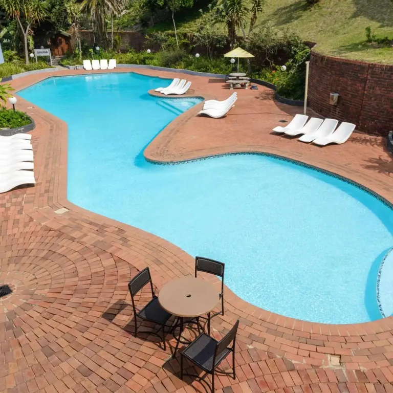 Piscine sinueuse entourée d'un sol pavé et de chaises longues.