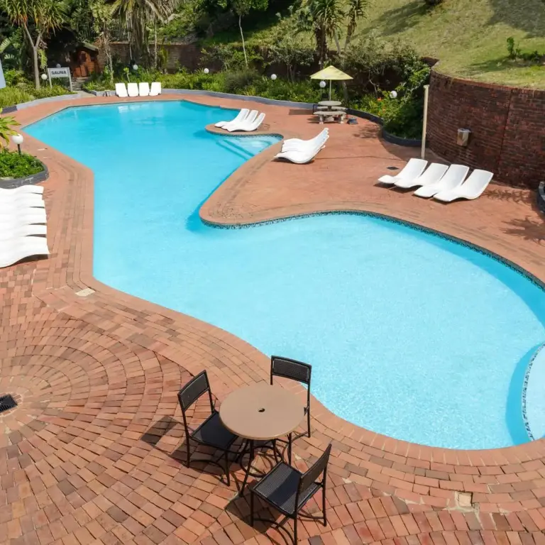 Piscine sinueuse entourée d'un sol pavé et de chaises longues.