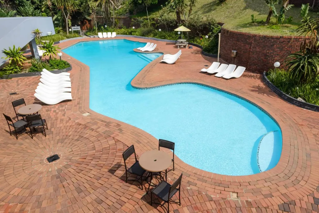 Une piscine turquoise sinueuse entourée d'une terrasse pavée et de chaises longues.