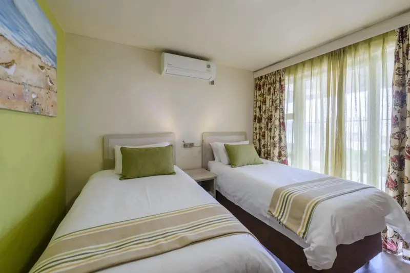 Une chambre lumineuse avec deux lits simples et des rideaux fleuris.