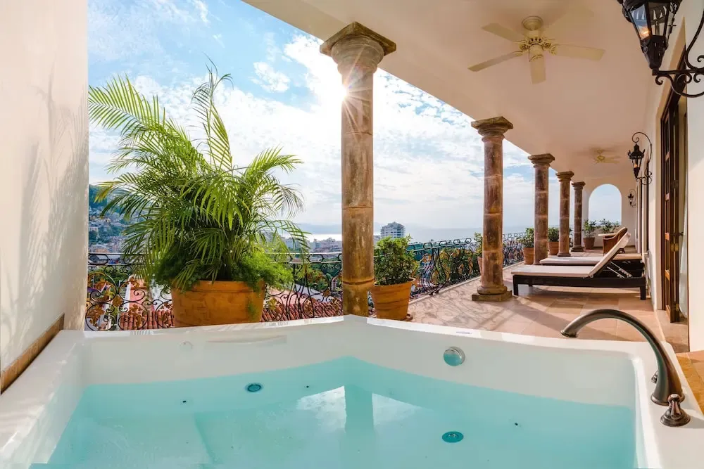 Un jacuzzi intégré à une terrasse avec vue sur la mer et la végétation.