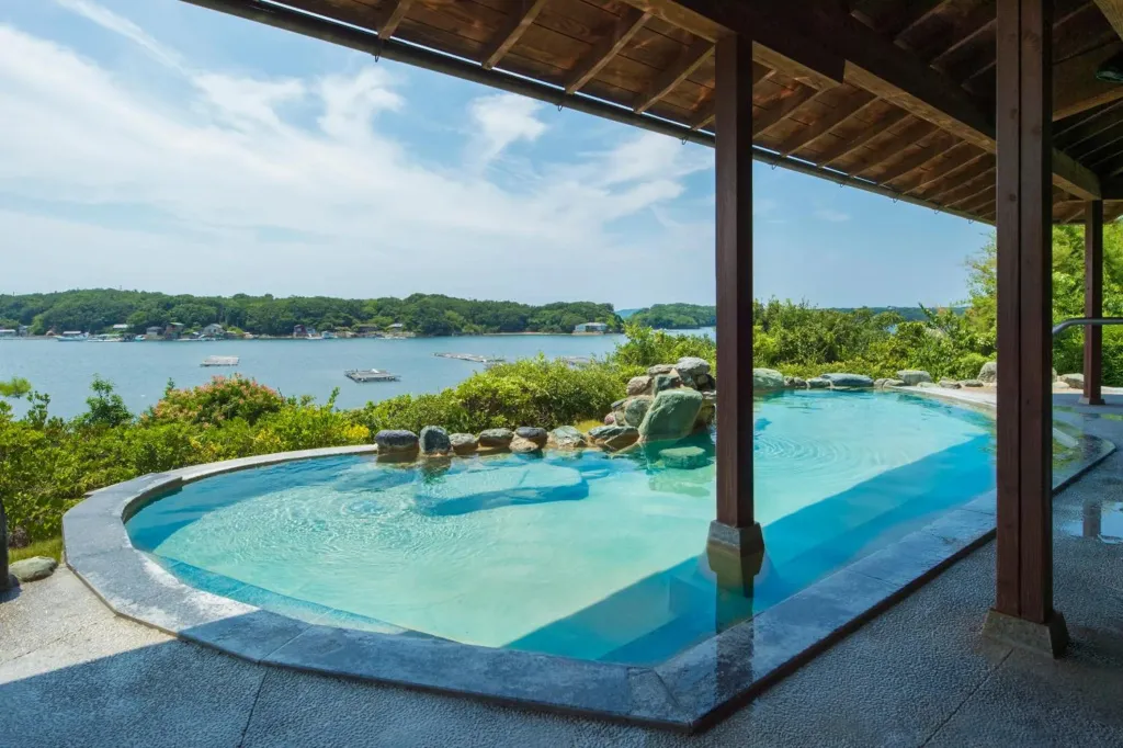 Une piscine extérieure avec un espace de détente ombragé offre une vue sur la mer et la végétation.