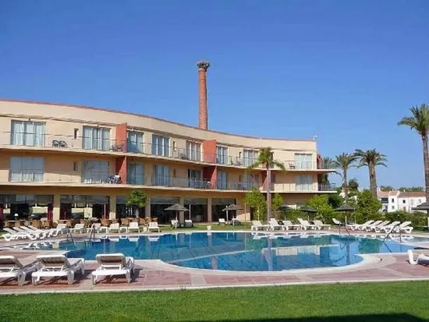 Bâtiment beige à plusieurs étages avec piscine et transats en contrebas.