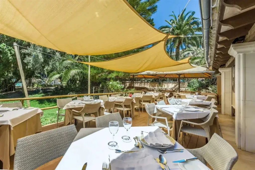 Une terrasse ombragée abrite des tables de restaurant dressées pour le service.