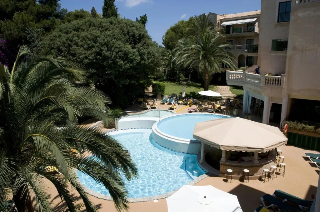 Une piscine avec un bar intégré et des transats dans un jardin luxuriant.