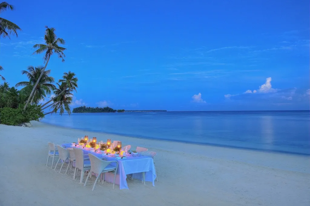 Une table dressée sur une plage de sable blanc au crépuscule.