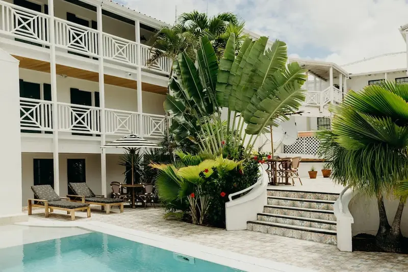 Transats et végétation luxuriante bordent une piscine turquoise devant un bâtiment blanc à balcons.