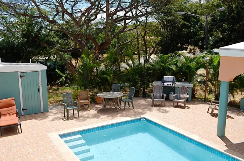 Une piscine turquoise est entourée d'une terrasse carrelée avec des meubles de jardin et un barbecue.