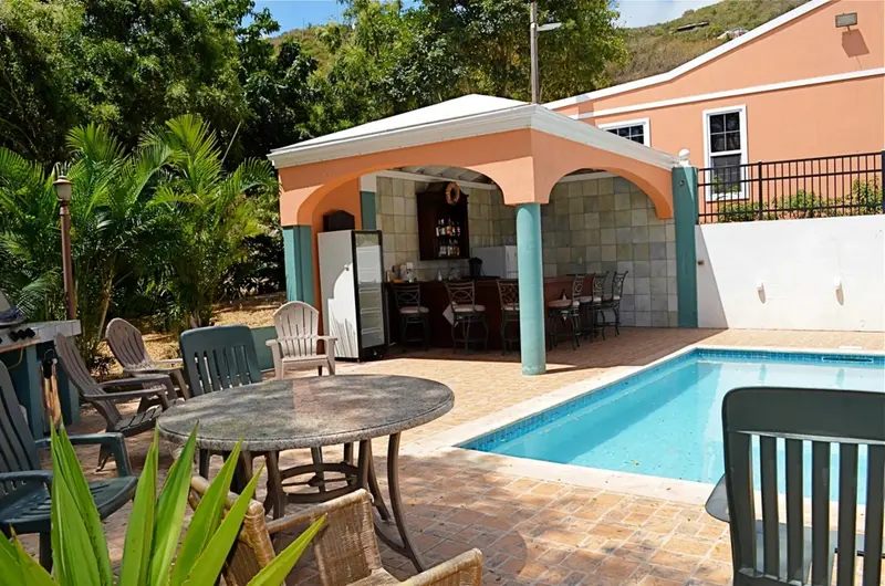 Terrasse ombragée avec bar et piscine ensoleillée.