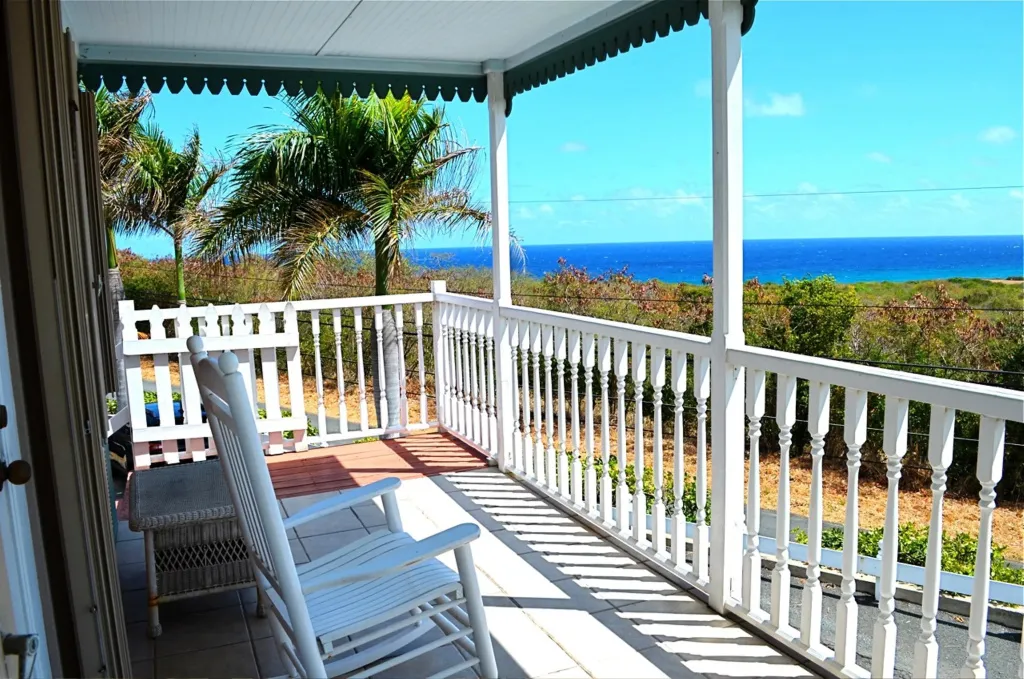 Terrasse en bois avec mobilier blanc donnant sur la mer et la végétation.