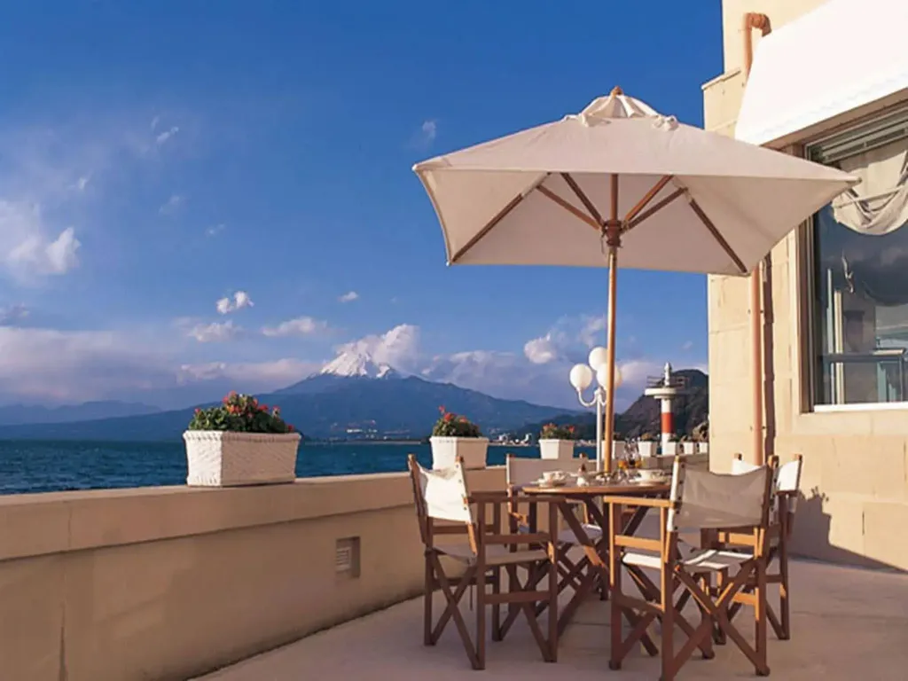 Une table à manger est placée sur une terrasse ensoleillée avec vue sur la mer et les montagnes.
