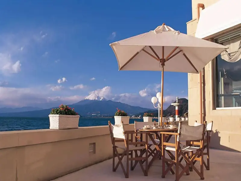 Une table à manger est placée sur une terrasse ensoleillée avec vue sur la mer et les montagnes.