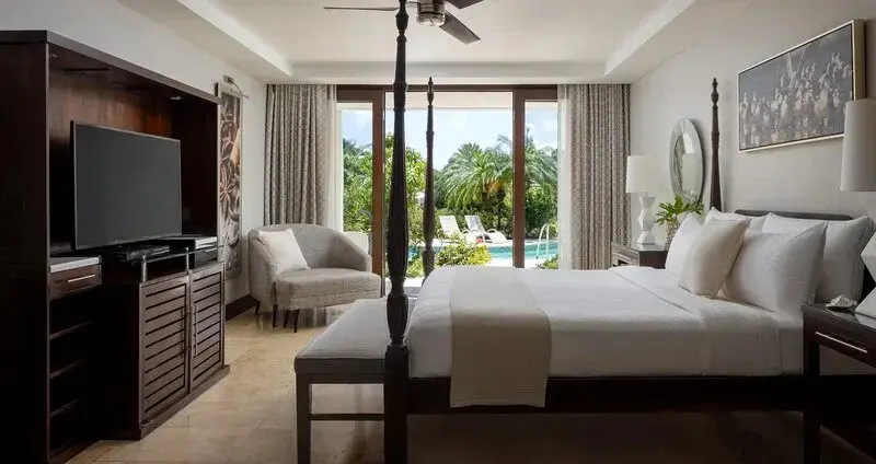 Une chambre lumineuse avec un grand lit et un coin salon donnant sur une piscine.