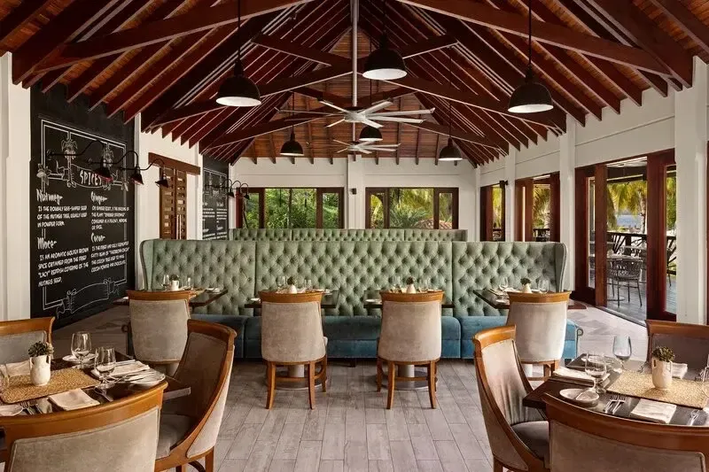 Une salle de restaurant lumineuse avec des tables dressées et un grand canapé vert.