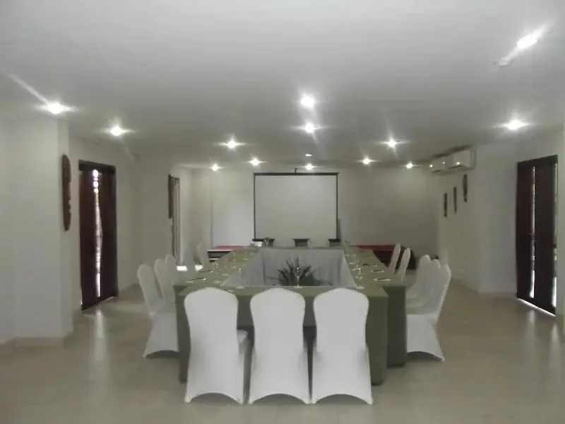 Une salle lumineuse est aménagée avec des tables et des chaises disposées en U.