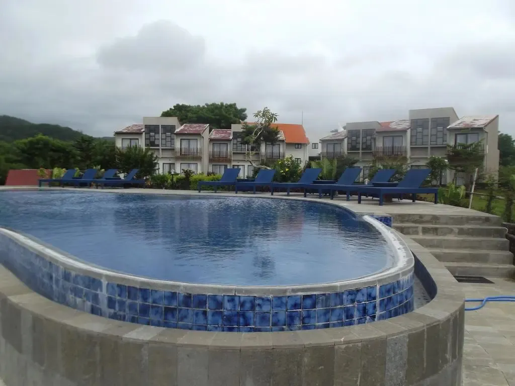 Piscine bleue bordée de transats devant des bâtiments blancs.