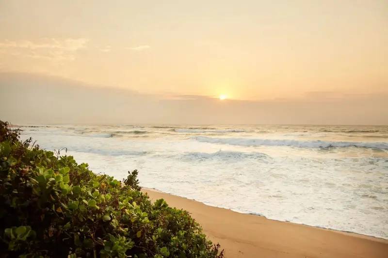 Le soleil se couche sur une plage de sable fin, avec des vagues déferlant sur le rivage.