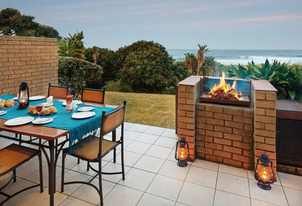 Une table de repas est dressée sur une terrasse avec vue sur la mer et une cheminée.