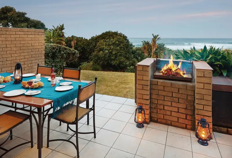 Une table de repas est dressée sur une terrasse avec vue sur la mer et une cheminée.