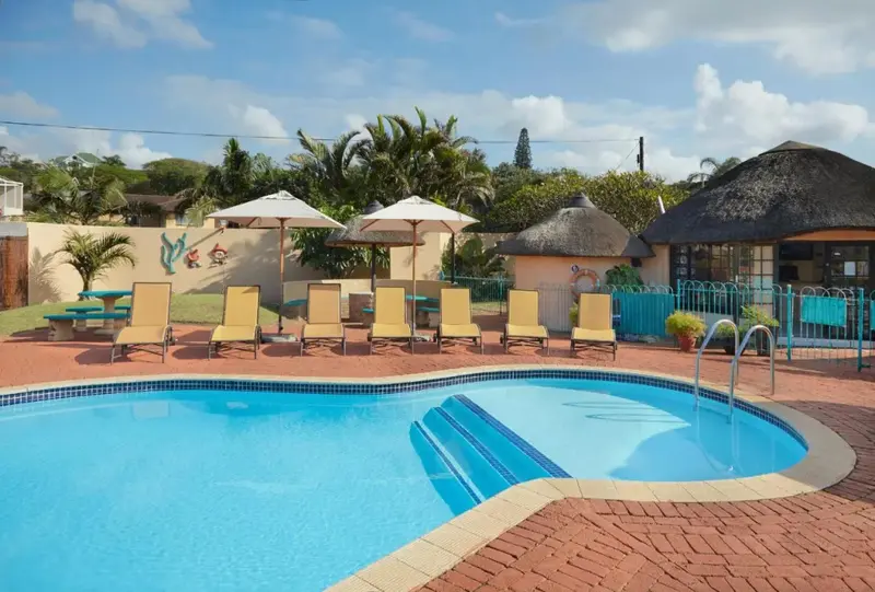 Piscine ensoleillée avec chaises longues et parasols dans un jardin tropical.