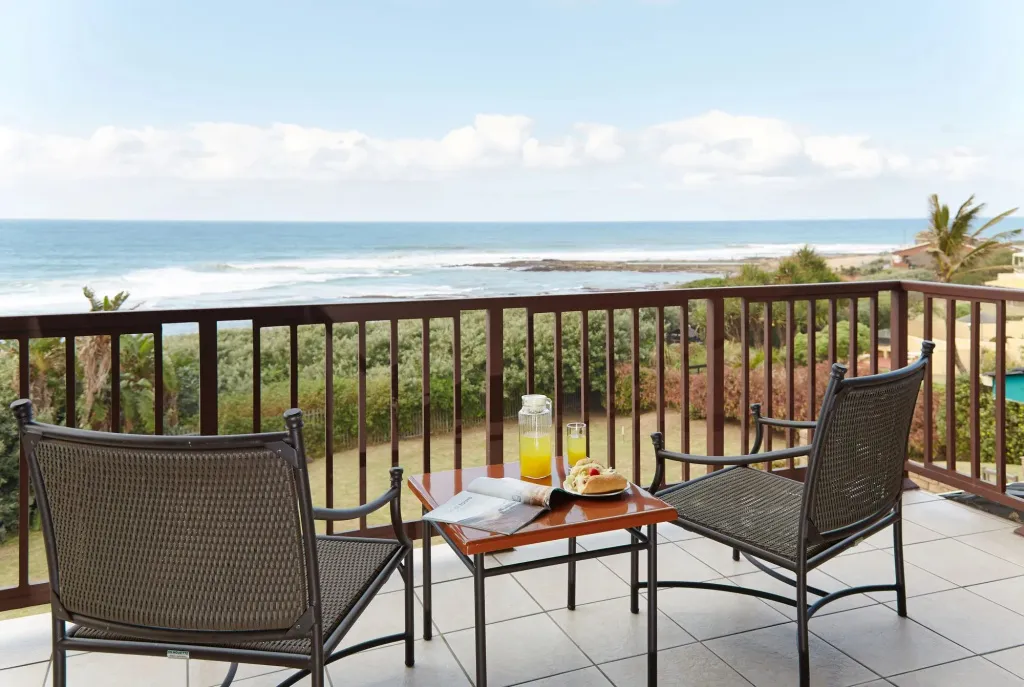 Deux fauteuils et une table basse avec un petit-déjeuner sont disposés sur une terrasse avec vue sur la mer.