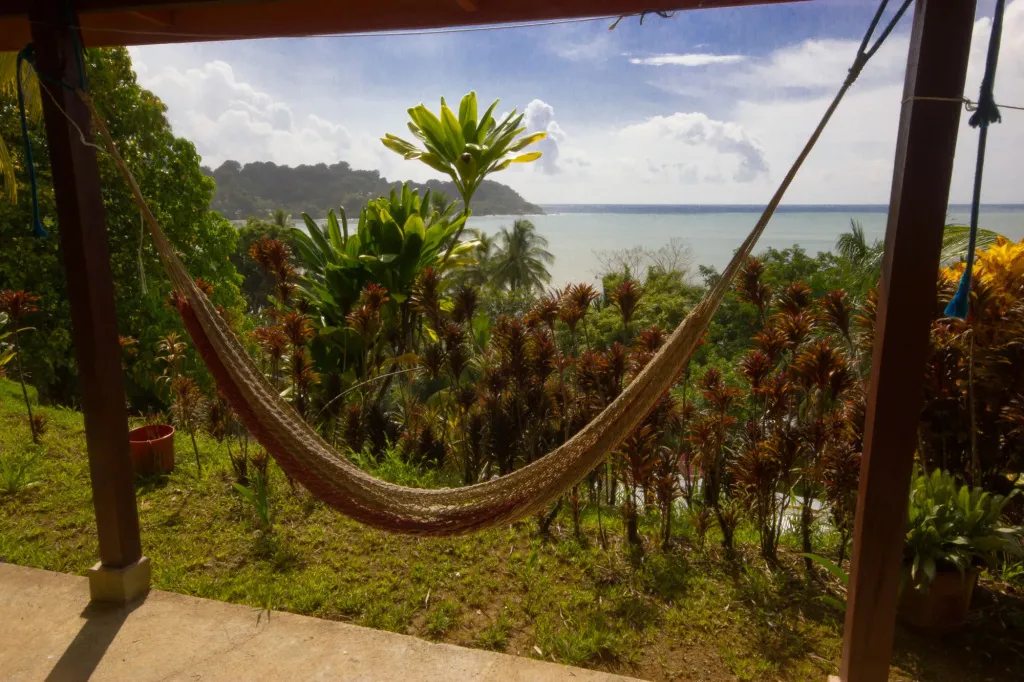 Un hamac est suspendu sur une terrasse avec vue sur la mer et la végétation tropicale.