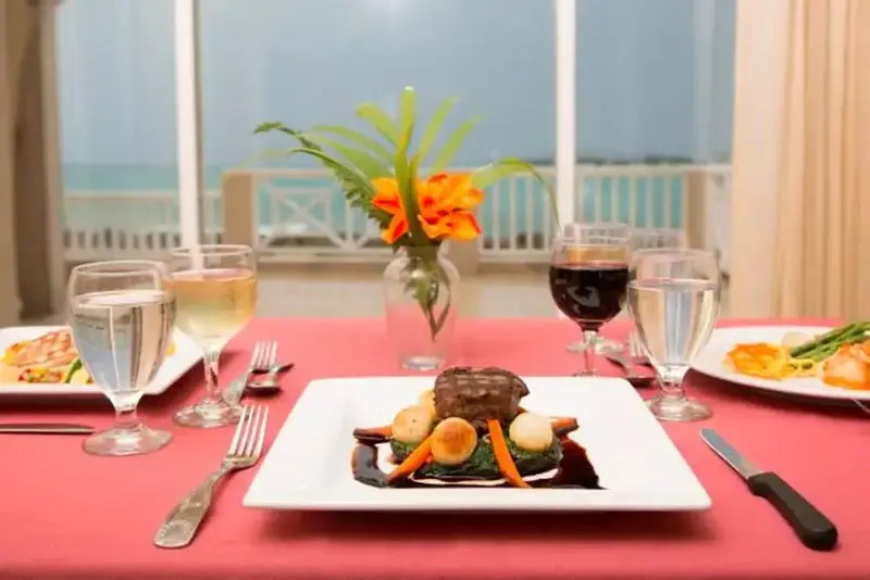 Une table est dressée avec des plats et des boissons devant une grande fenêtre donnant sur la mer.