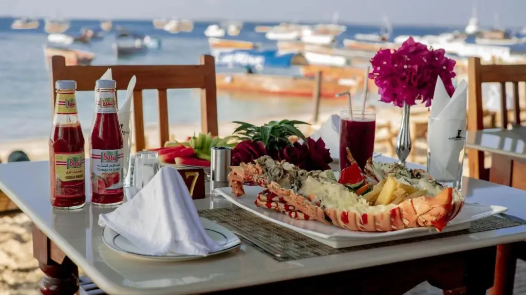 Une table dressée avec un plat de fruits de mer et des boissons face à la mer.